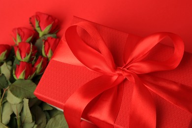 Beautiful gift box with bow and roses on red background, closeup