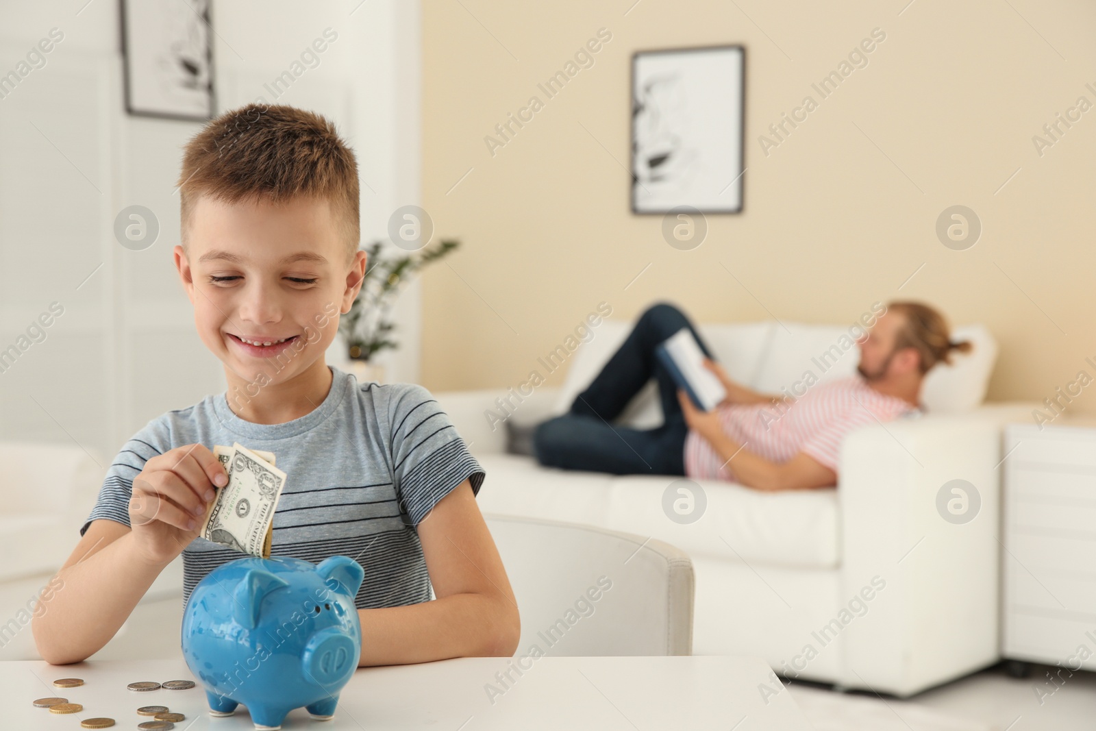 Photo of Boy putting money into piggy bank on table indoors. Space for text