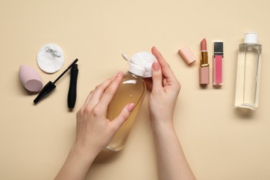 Woman using makeup remover, closeup. Cleanser, cotton pads, lipstick, lip gloss, mascara and sponge on beige background, top view