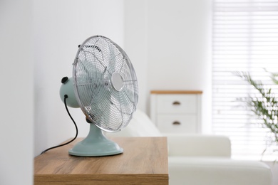 Photo of Modern electric fan on wooden table indoors. Space for text