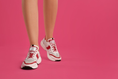 Woman wearing sneakers on pink background, closeup. Space for text