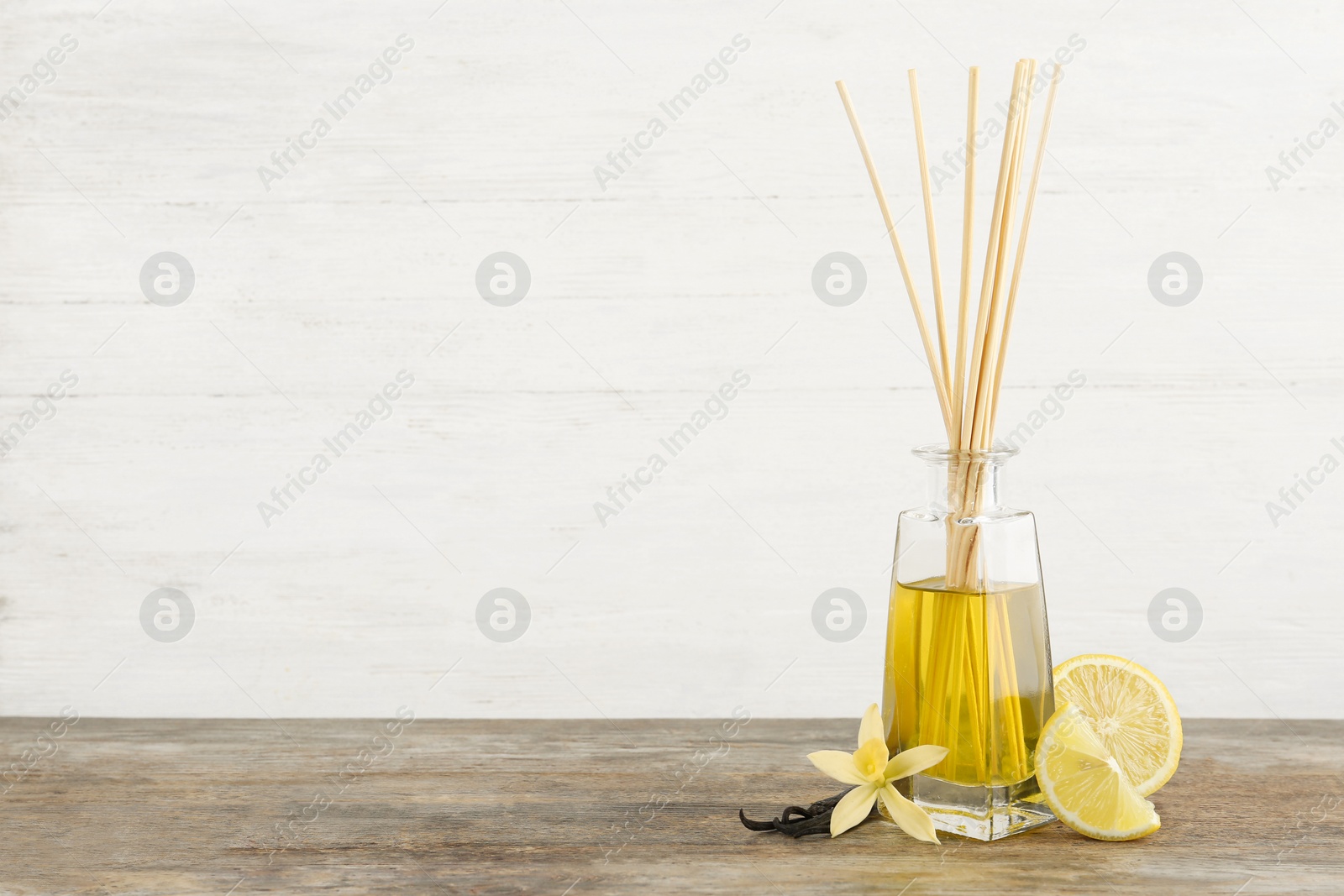 Photo of Aromatic reed freshener, lemon and vanilla on wooden table against light background. Space for text