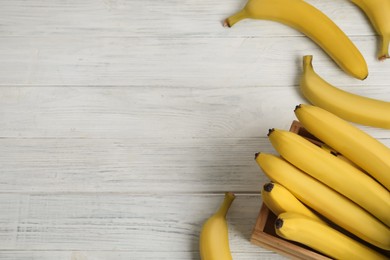 Ripe yellow bananas and crate on white wooden table, flat lay. Space for text