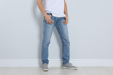 Young man in stylish jeans near light wall, closeup