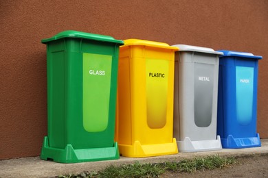 Photo of Many color recycling bins near brown wall outdoors