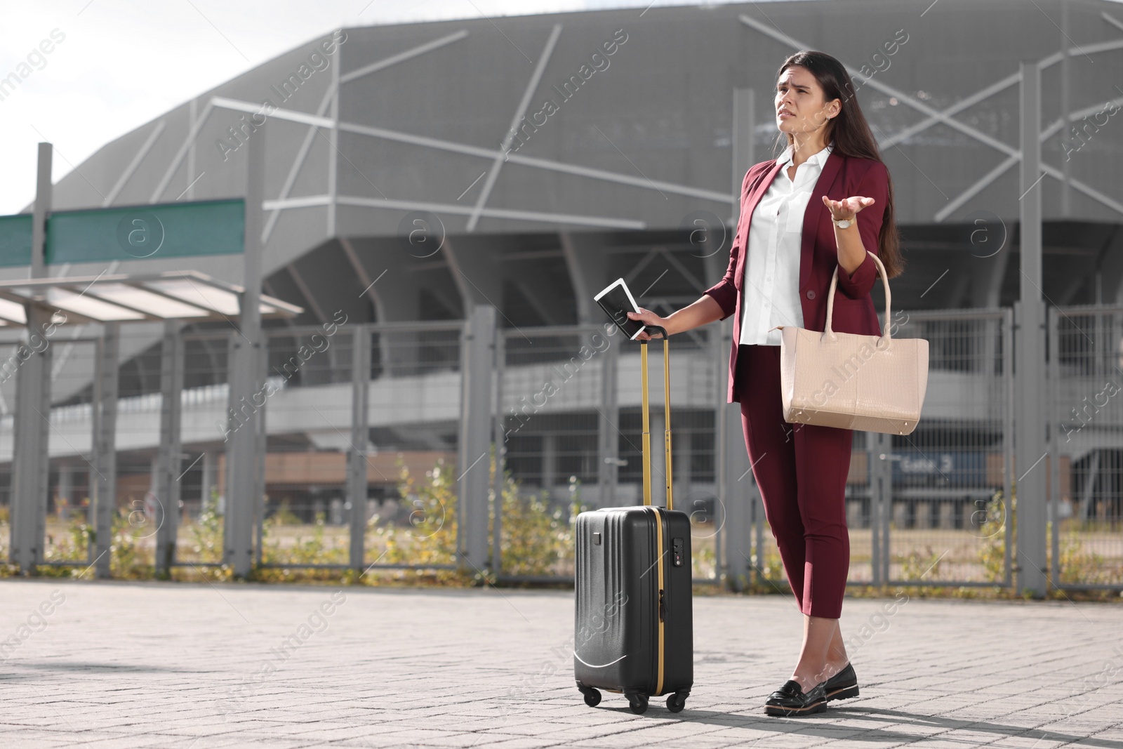 Photo of Being late. Worried businesswoman with black suitcase and passport outdoors, space for text