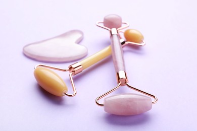 Gua sha stone and different face rollers on violet background