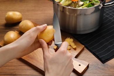 Woman peeling potato for cooking tasty bouillon at wooden table, closeup