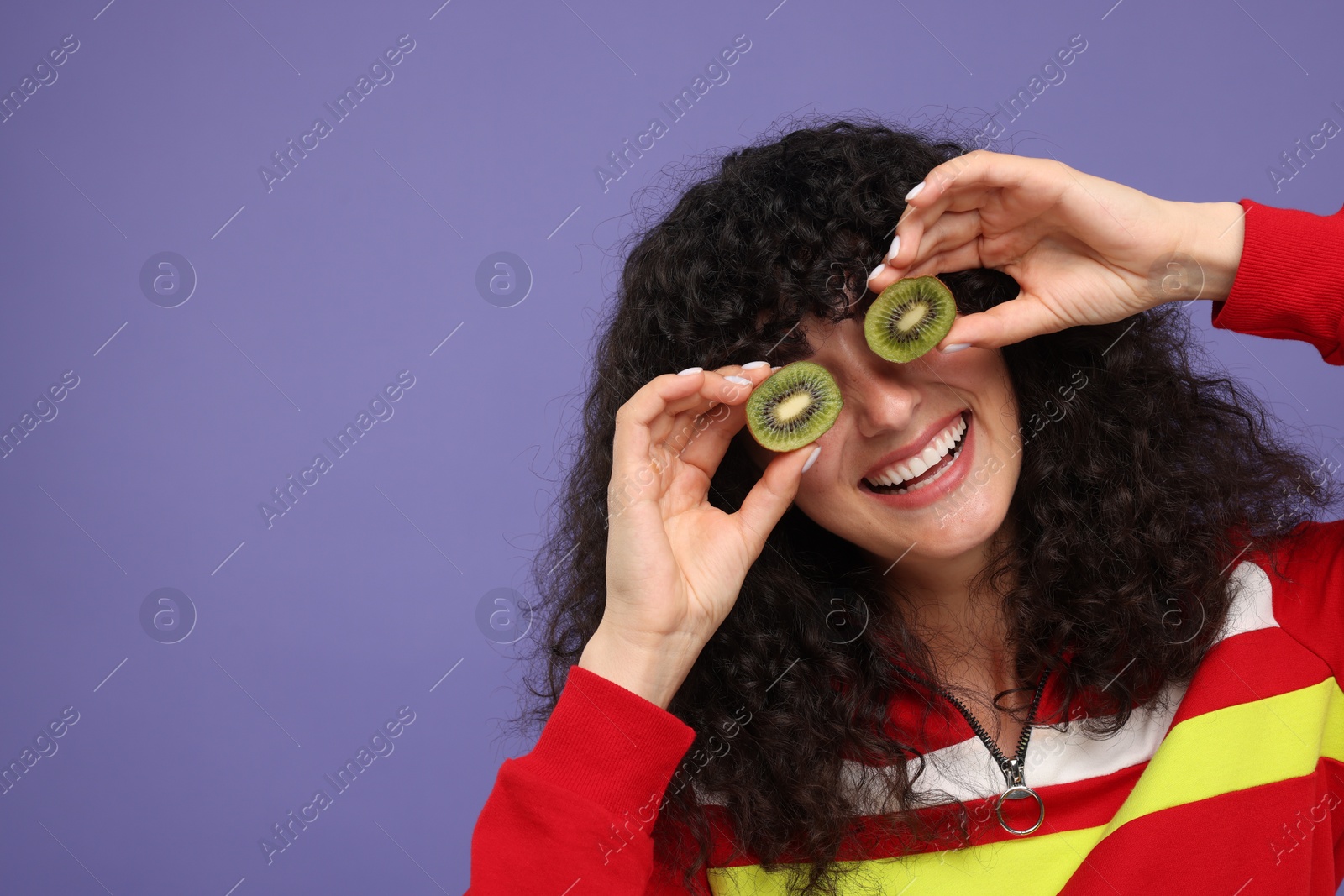 Photo of Woman covering eyes with halves of kiwi on violet background, space for text