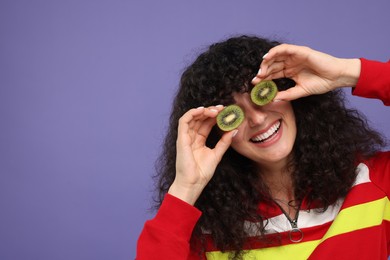Photo of Woman covering eyes with halves of kiwi on violet background, space for text