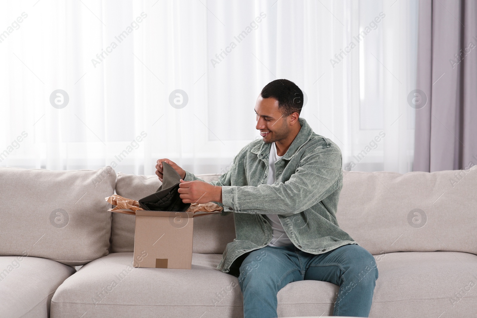 Photo of Happy young man opening parcel at home. Internet shopping