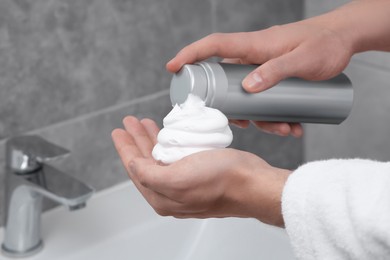 Photo of Man applying shaving foam onto hand in bathroom, closeup