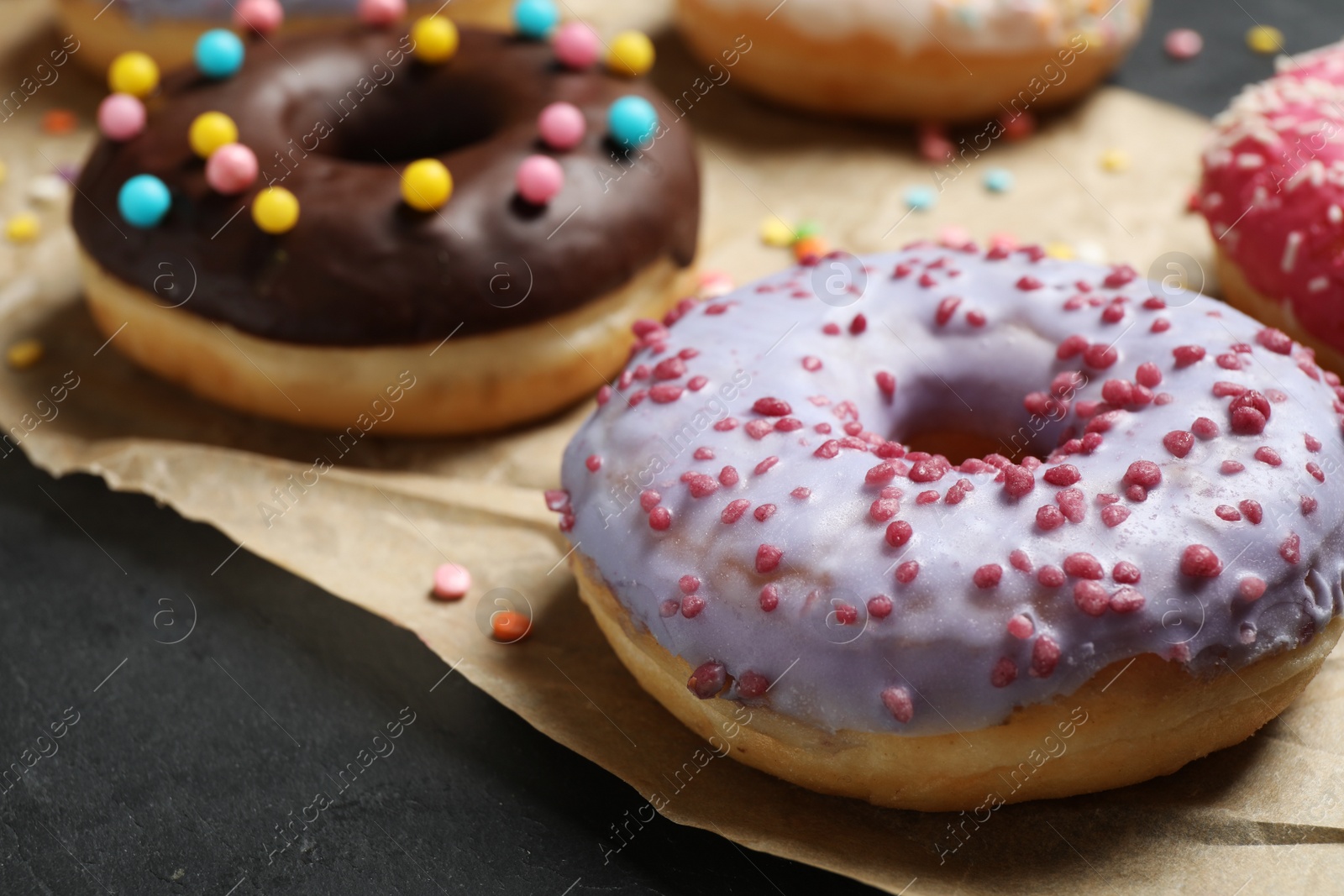 Photo of Yummy donuts with sprinkles on dark background, closeup