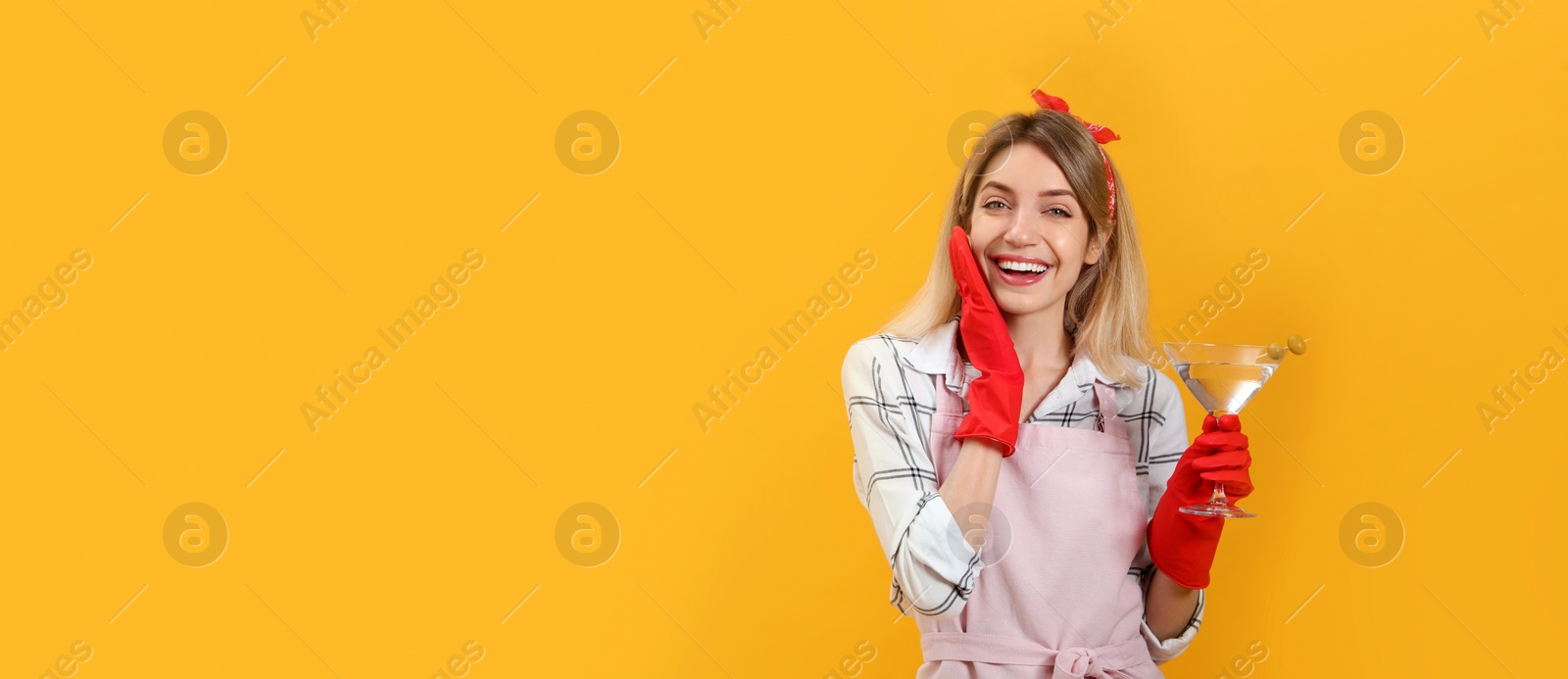 Photo of Young housewife with glass of martini on yellow background. Space for text
