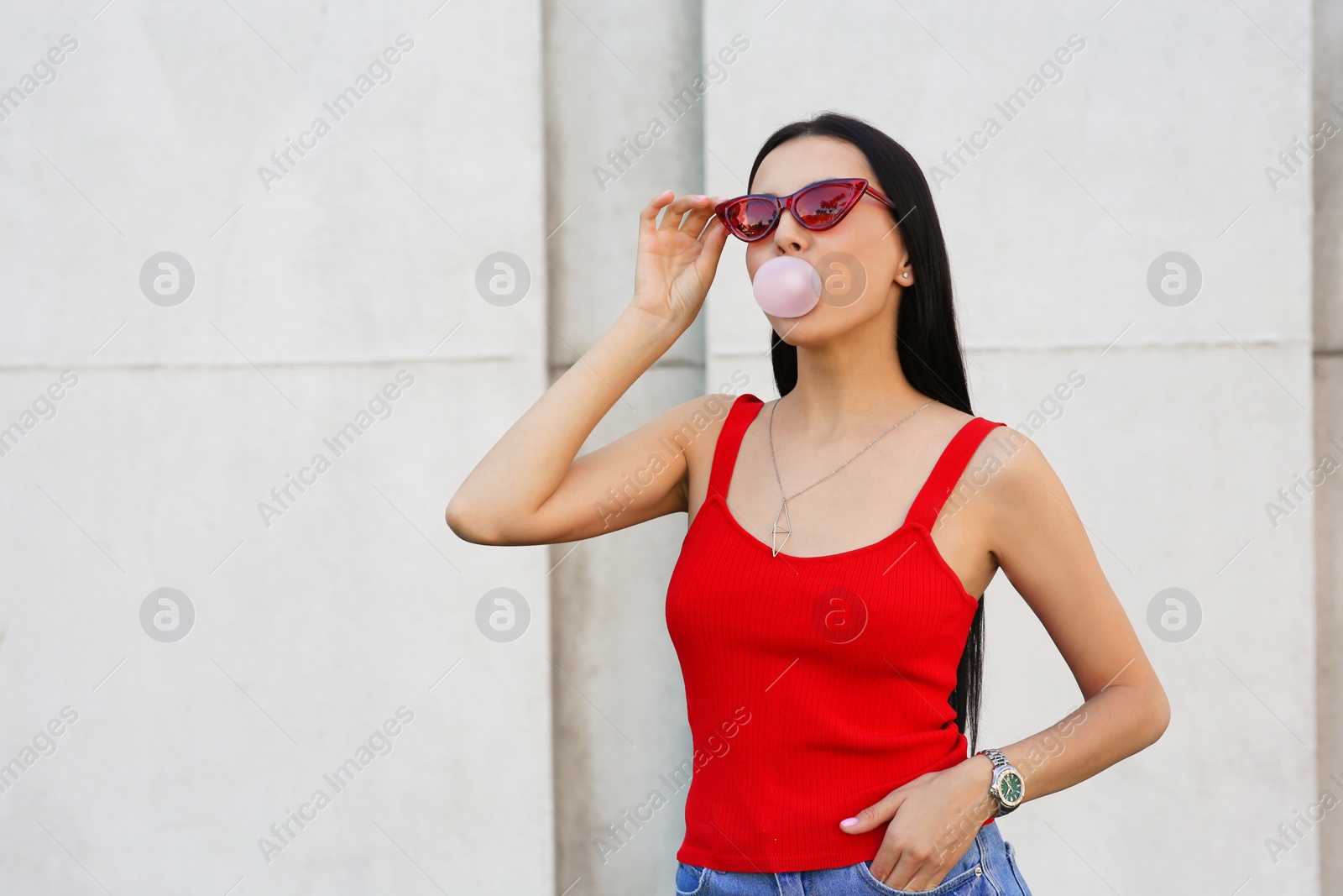 Photo of Beautiful woman in stylish sunglasses blowing gum near wall outdoors, space for text