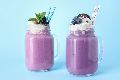 Tasty milk shakes in mason jars on light blue background