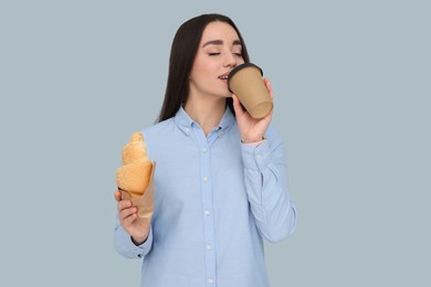 Photo of Young female intern with croissant and cup of drink on grey background