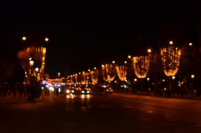 Photo of Blurred view of street with beautiful lights on trees and cars at night. Bokeh effect