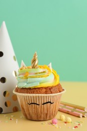Photo of Cute sweet unicorn cupcake and party items on yellow table
