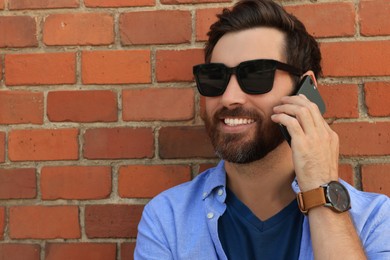 Happy man talking on phone near red brick wall. Space for text