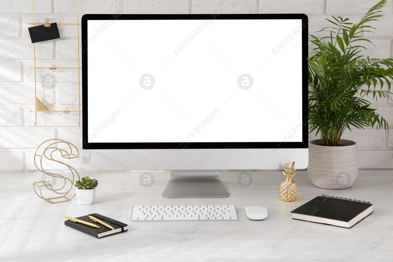 Photo of Office workplace with computer, stationery and decor on light table near white brick wall