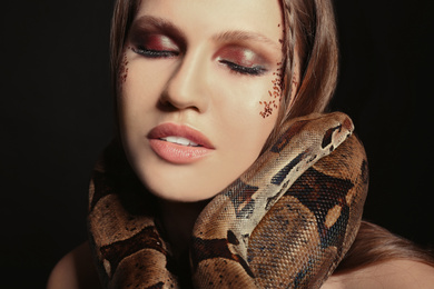 Photo of Beautiful woman with boa constrictor on black background, closeup