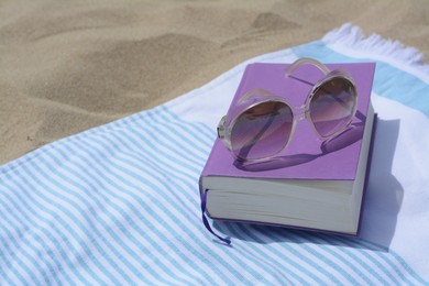 Photo of Beach towel with book and sunglasses on sand, space for text