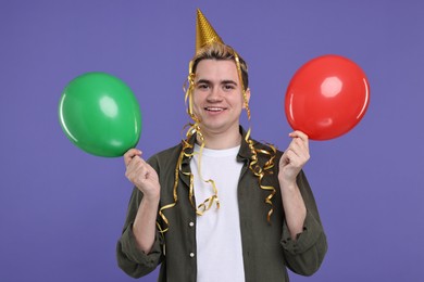 Young man with party hat and balloons on purple background