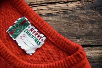 Photo of Christmas sweater with tag on wooden background, closeup