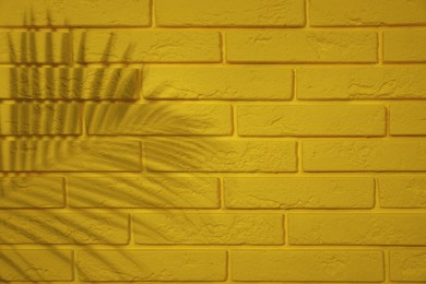 Shadow of tropical palm leaf on yellow brick wall, space for text