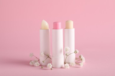 Different lip balms and gypsophila on pink background