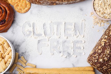 Photo of Frame of different products and phrase Gluten free written with flour on white marble table, flat lay