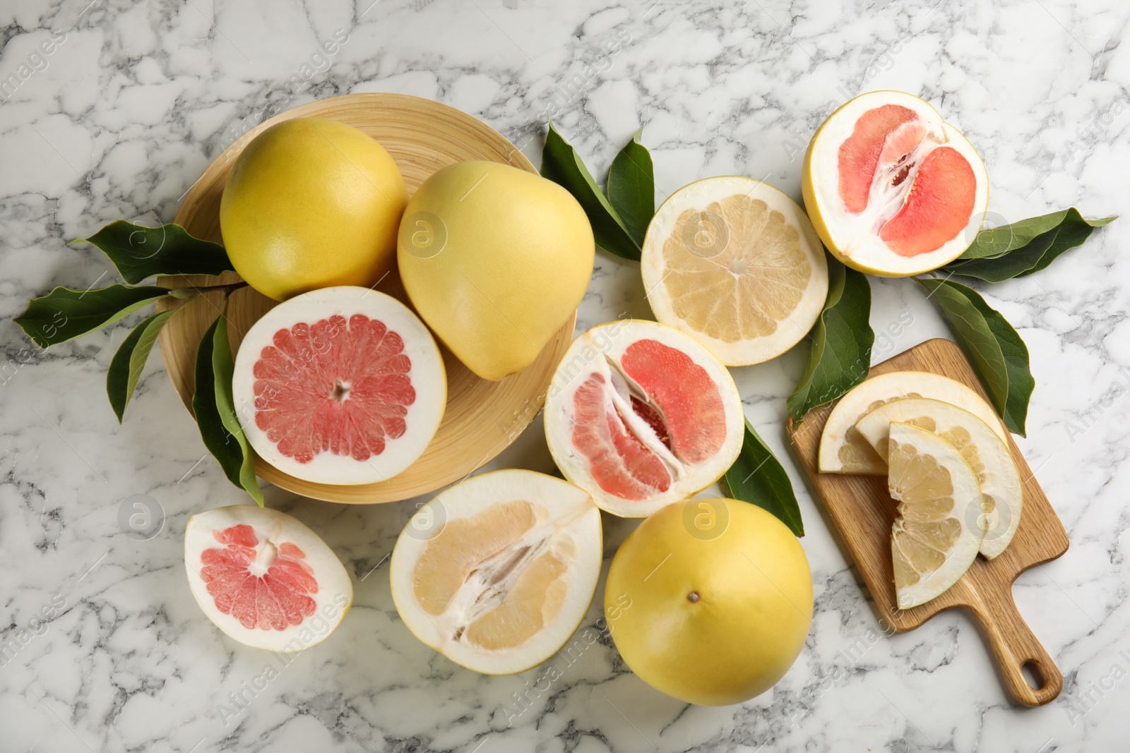 Photo of Fresh cut and whole pomelo fruits with leaves on white marble table, flat lay