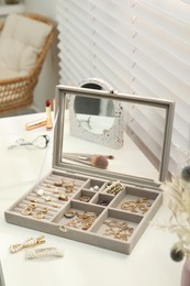 Elegant jewelry box with beautiful bijouterie and makeup products on dressing table indoors