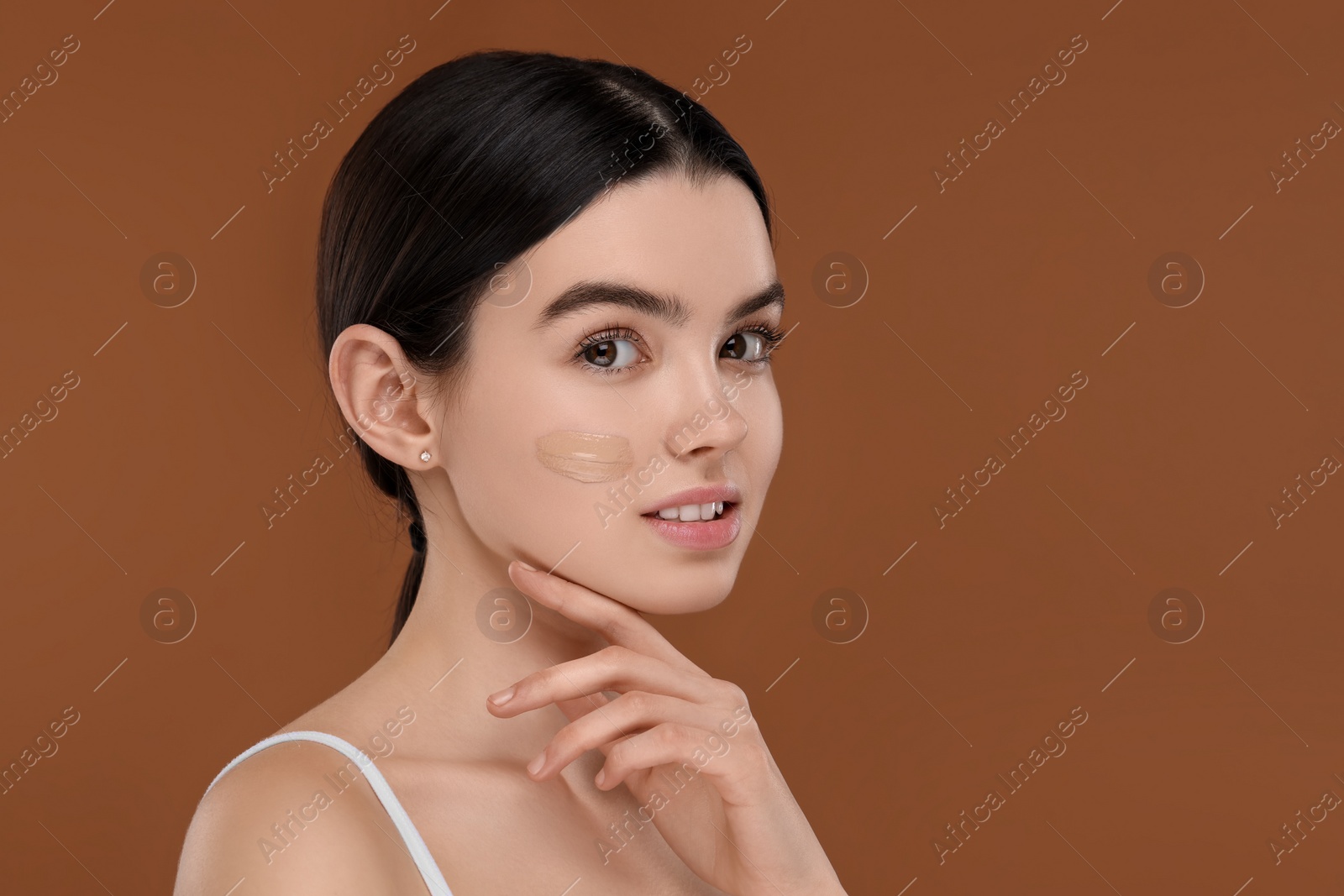 Photo of Teenage girl with swatch of foundation on face against brown background. Space for text