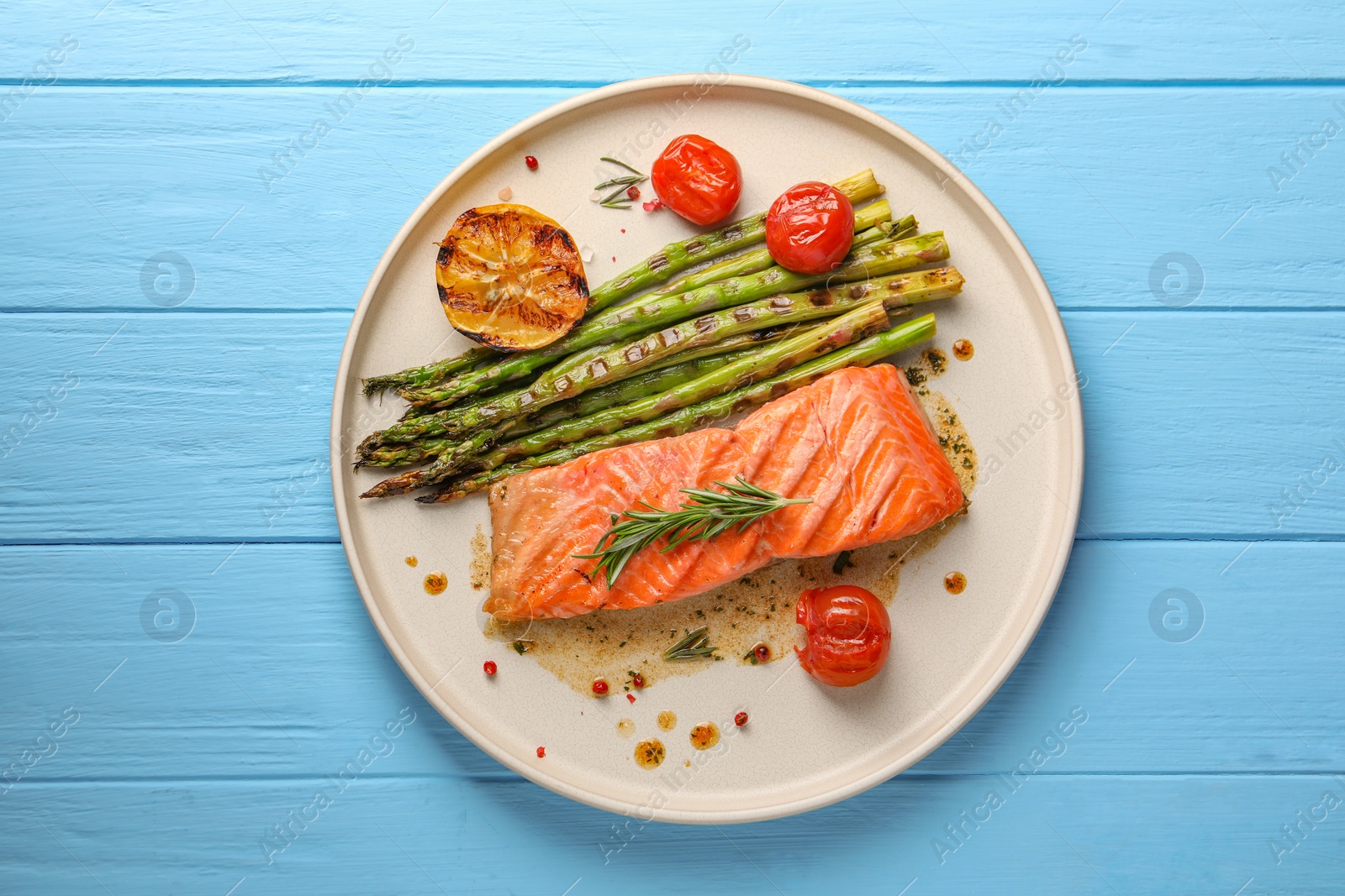 Photo of Tasty grilled salmon with tomatoes, asparagus and spices on light blue wooden table, top view