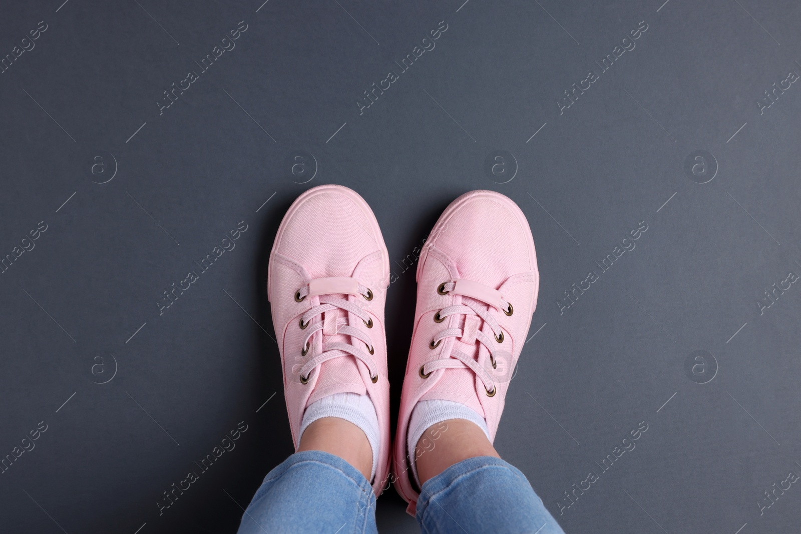 Photo of Woman in stylish sneakers standing on grey background, top view