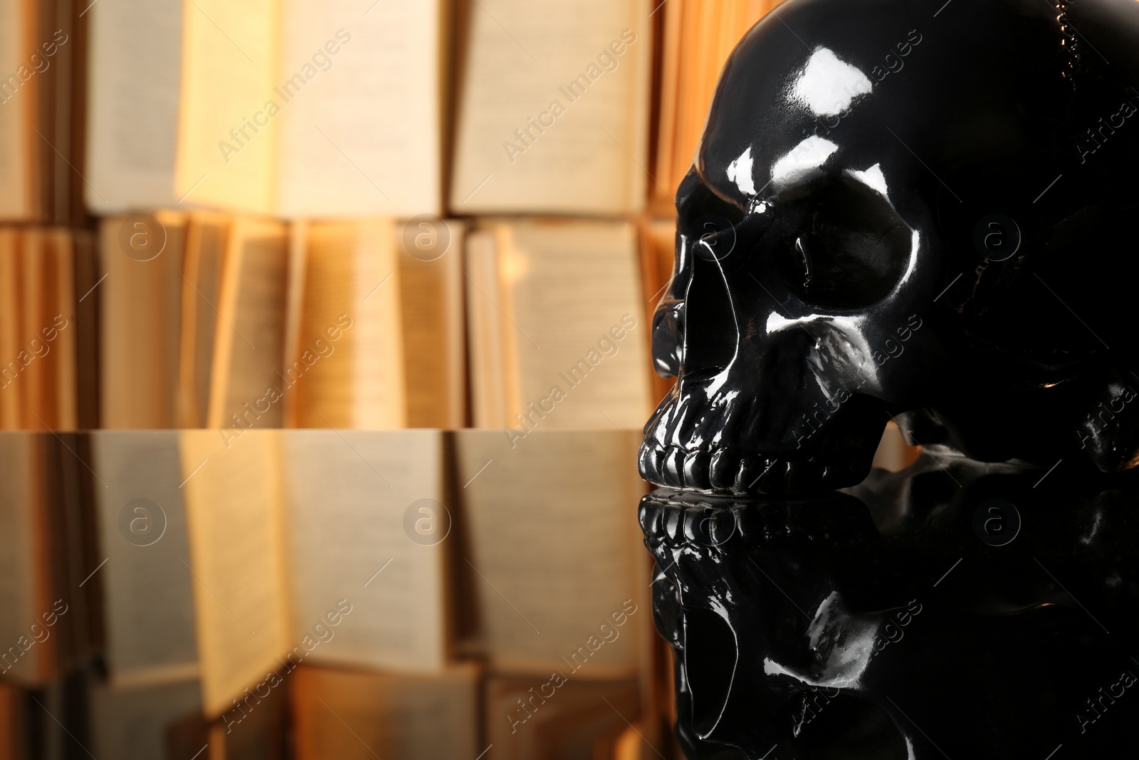 Photo of Black human skull on mirror table near books. Space for text