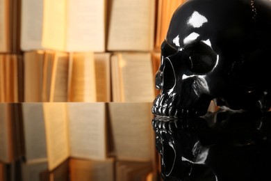 Photo of Black human skull on mirror table near books. Space for text