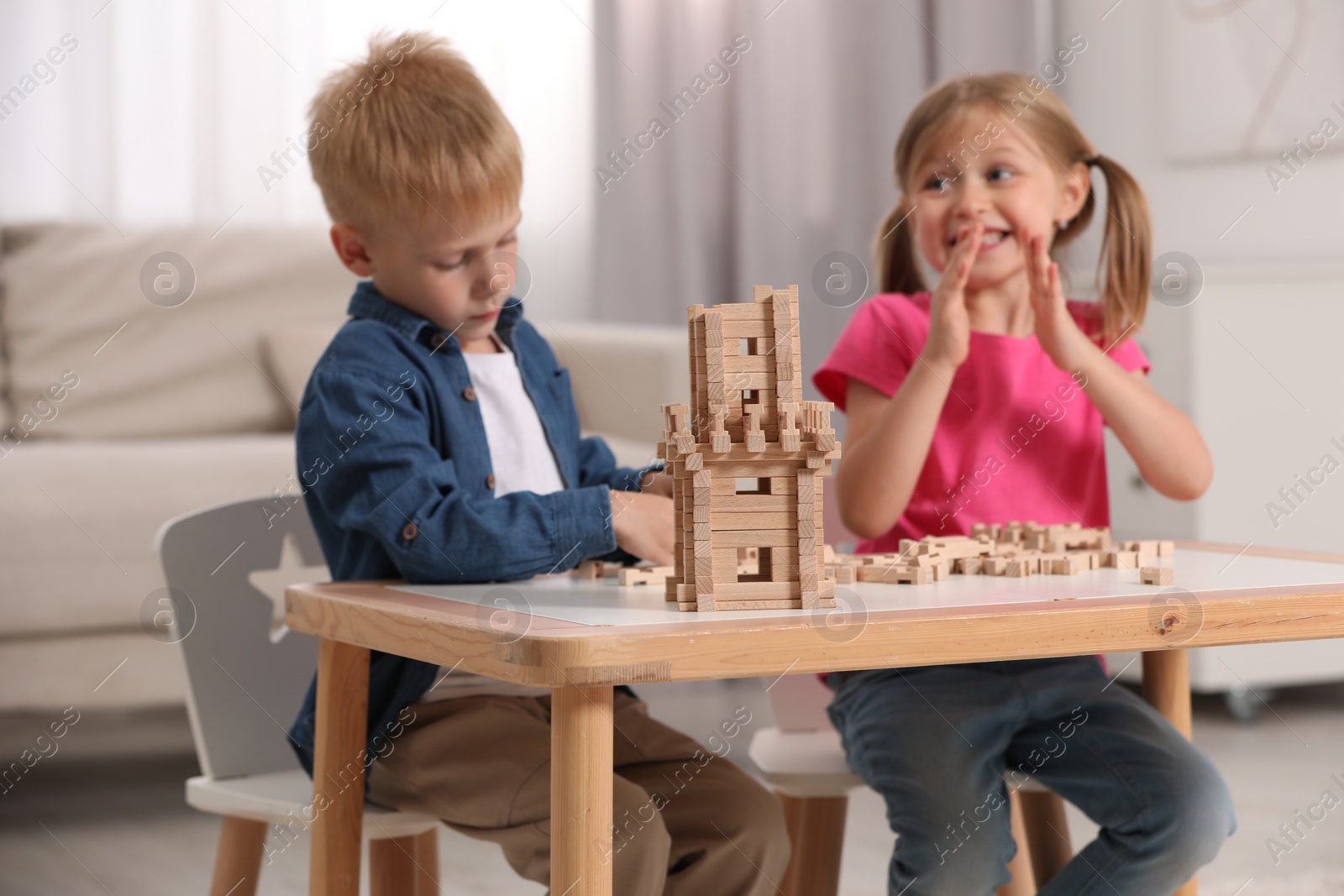Photo of Little girl and boy playing with wooden tower at table indoors, selective focus. Children's toy