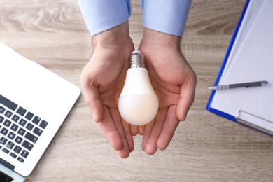 Photo of Man holding lamp bulb over table with laptop, top view