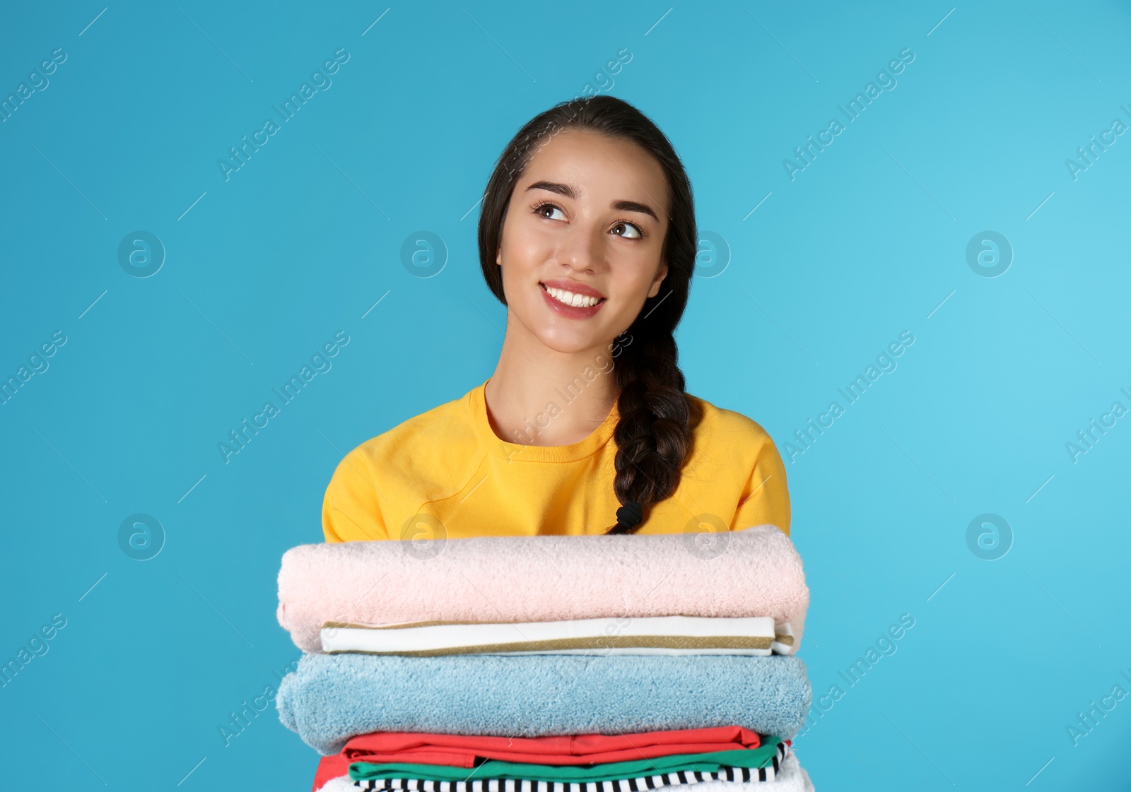 Photo of Happy young woman holding clean laundry on color background