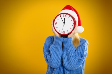 Woman in Santa hat with clock on yellow background, space for text. New Year countdown