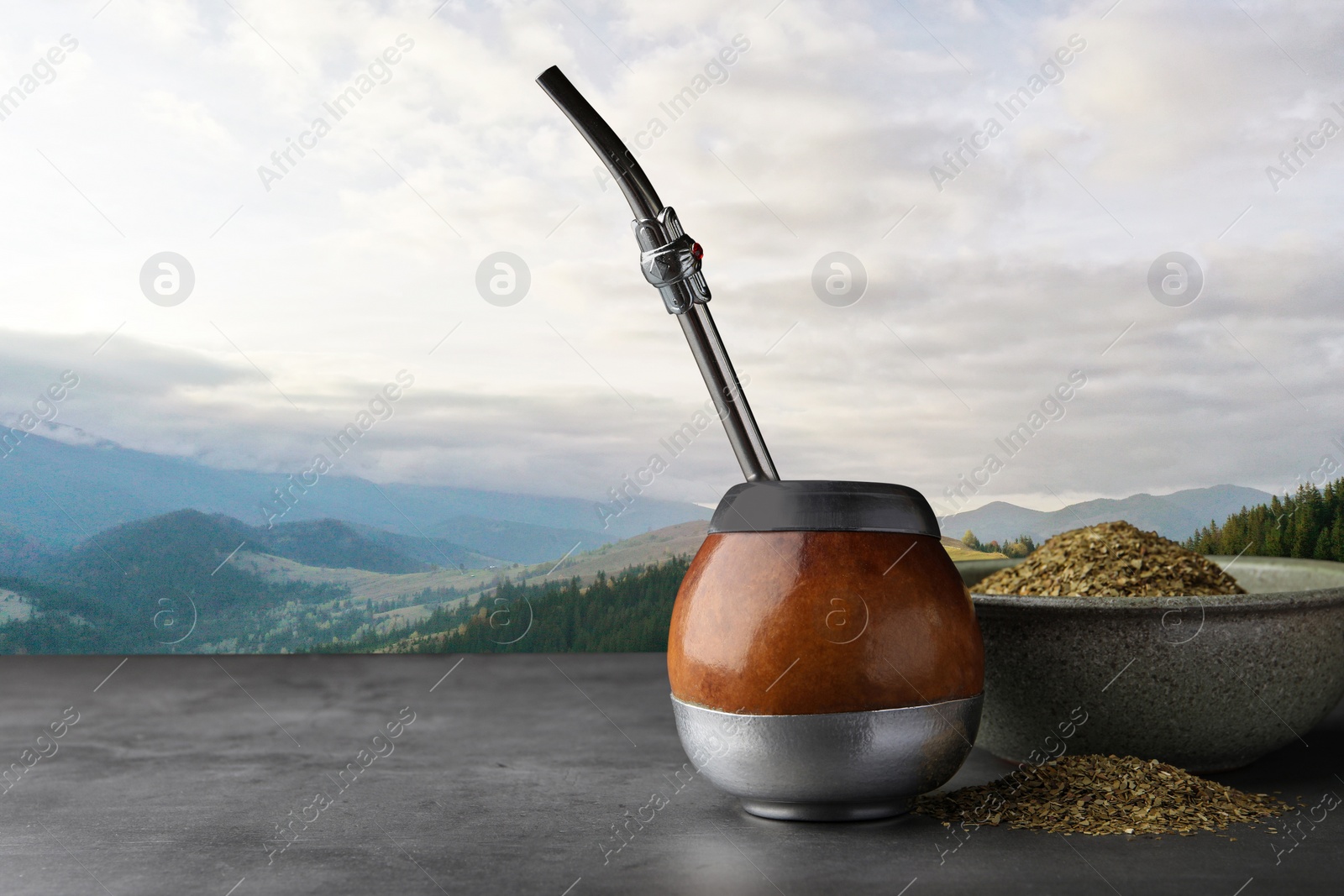 Image of Calabash with mate tea and bombilla on light grey table and beautiful view of mountain landscape, space for text