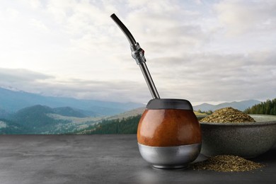 Calabash with mate tea and bombilla on light grey table and beautiful view of mountain landscape, space for text