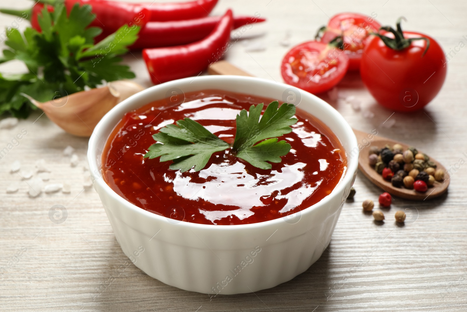 Photo of Spicy chili sauce with parsley in bowl on white wooden table