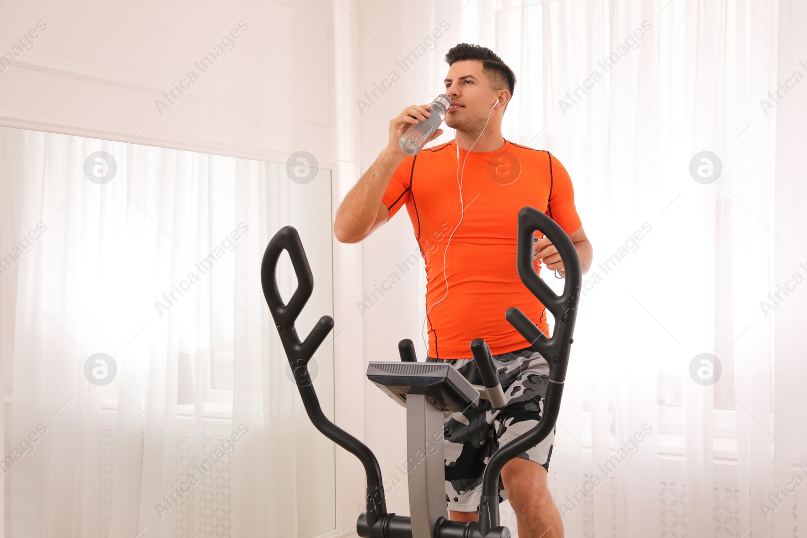 Photo of Man drinking water on elliptical machine at home