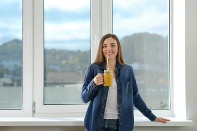 Photo of Beautiful young woman with delicious smoothie near window