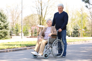 Photo of Senior woman in wheelchair and mature man at park on sunny day