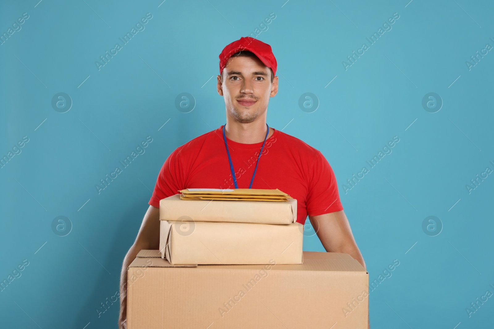 Photo of Happy young courier with parcels and envelopes on blue background